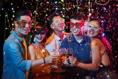 happy excited young vietnamese people in party glasses posing with champagne glasses under fallling confetti