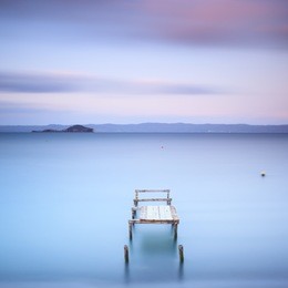 wooden pier or jetty on a blue lake. hills on background. long exposure photography in bolsena lake, italy, europe.