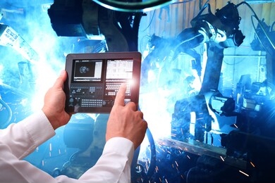 industry 4.0 ,  concept  of man hand holding cell phone or tablet with augmented reality screen software and blue tone of automate wireless robot arm in smart factory background. mixed media