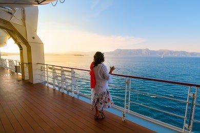 a woman sips a drink on the deck of a cruise ship as the sun sets and the ship passes islands on the aegean sea