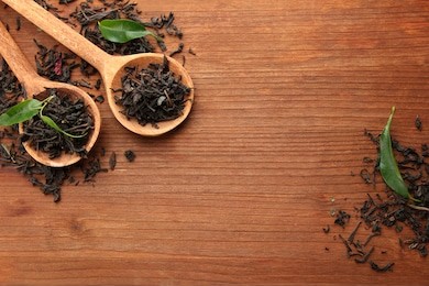 dry tea with green leaves in wooden spoons, on wooden background