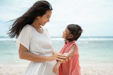 mother rub a sunblock to daughter's skin on the seashore at midday