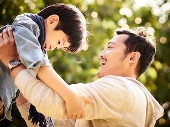 asian father having fun lifting son oudoors in park.
