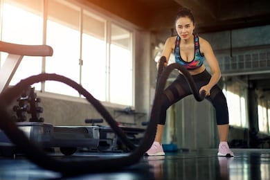 asian woman doing training battle rope exercise in fitness gym. female taking weight loss with machine aerobic for slim and firm health. healthy sport cardio strong.
