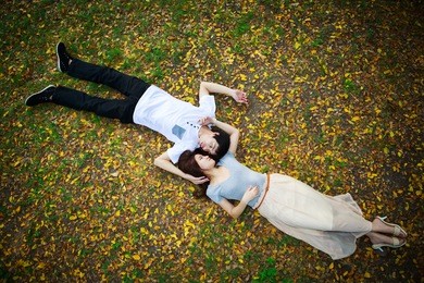 asian couple laying down outdoor in park looking happy on fall ground