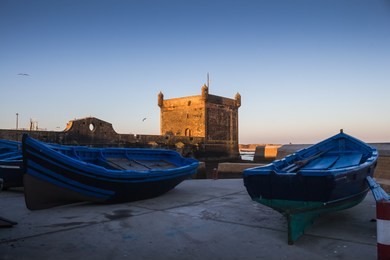 wooden fishing boats in a port. tower of the fortification in the bacground. blue morning sky. essaouira, morocco.