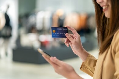 closeup asian woman using credit card with mobile for online shopping in department store over the clothes shop store background, technology money wallet and online payment concept, credit card mockup
