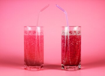 food on neon pink background. two glasses of homemade mix berry smoothie with straws. organic healthy beverage made of milk and fruit. concept for romance, love and st. valentine's day celevration.
