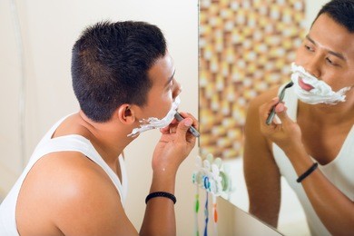 asian man shaving in front of bathroom mirror