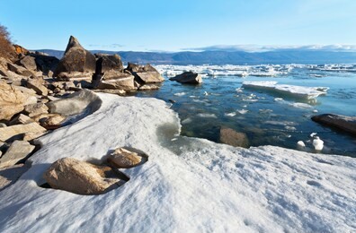lake baikal at spring day. view on the coast of the olkhon island and the white big ice floes on stony beach. nature background