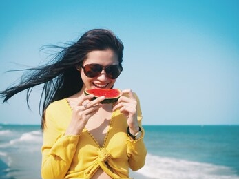 attractive young asian woman standing by the sea,she holding fresh watermelon,tropical summer concept.