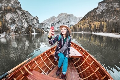 happy asian woman taking selfie with smartphone in a boat in a mountain lake during fall season