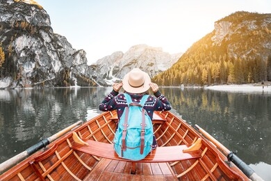 happy asian woman sitting in wooden vintage boat floating and sailing on a braies lake in italian alps mountains, travel and dream vacation concept