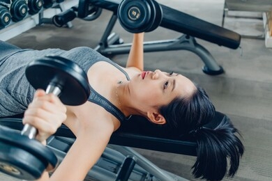 asian woman workout for dumbbell bench press in the fitness gym.
