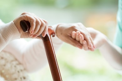 closeup of elderly lady holding walking cane in one hand and holding volunteer's hand in the other