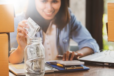 asia woman putting us dollar banknotes money  into  the glass bottle for saving money.