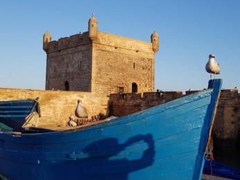 blue boat with photographer's shadow against the background of fort illuminated with morning light.