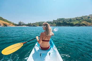 woman paddling a kayak by the tropical beach. kayaking tour in phuket, thailand