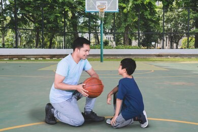 picture of young man teaching his son to play basketball while kneeling in the basketball court
