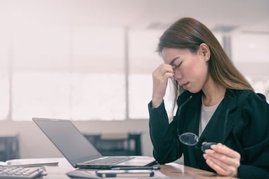 tired and stressed asian business woman closed eyes massaging nose and sitting at desk in front of laptop at office background