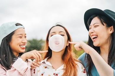 happy asian friends having fun chewing bubble gum outdoor - young people playing and laughing together - friendship, millennial generation and youth lifestyle concept 