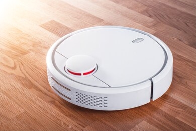 black robotic vacuum cleaner runs on laminate and on tile floor on sunny day. robot controlled by voice commands for direct cleaning. modern smart appliance for cleaning house.