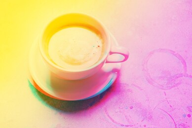 white cup fresh coffee scattered grains unhealthy food top view. toned vibrant neon colors yellow violet background