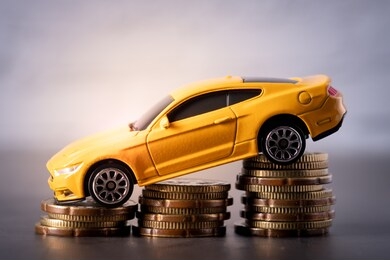 toy car on stacked coins concept of drop in sales, insurance, price, maintenance cost etc.