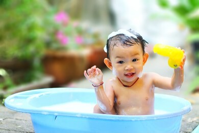 happy baby asian girl take a bath with bubbles soap and playing a duck toy. she sitting in a bathtub.