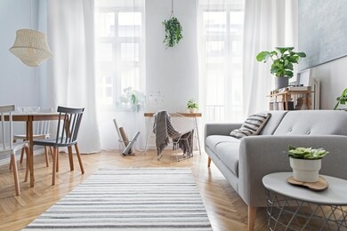 modern scandinavian living room with design furniture, family table, plants, bamboo bookstand and wooden desk. brown wooden parquet. abstract painting on the white wall. nice apartment. 