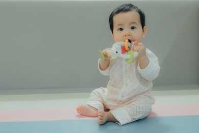 asian baby is chewing on teething toy. baby girl is teething , chewing toy.