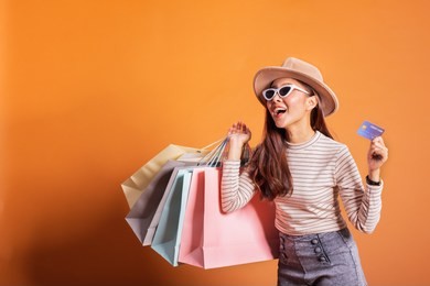 young beautiful fashionable asian woman holding shopping bags phone and credit card over orange background studio shot