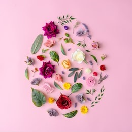 easter egg shape made with various spring flowers and leaves on pastel pink background. minimal happy easter concept. flat lay.