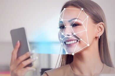 smiling blonde businesswoman using smartphone with face recognition technology in blurred office. toned image double exposure