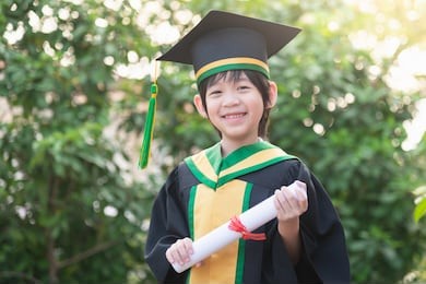 happy asian child in graduation gowns holding a certificate.graduation concept