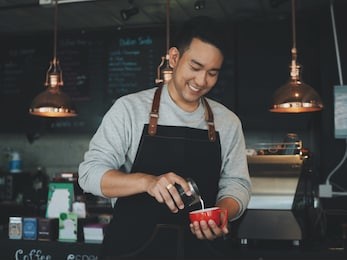 attractive asian man making coffee in his cafe.