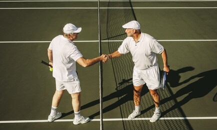 side view of two senior tennis players shaking hands on tennis court. senior men on a tennis court standing near the net shaking hands.