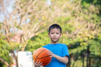 asian boy holding a basketball ball background blurry trees.