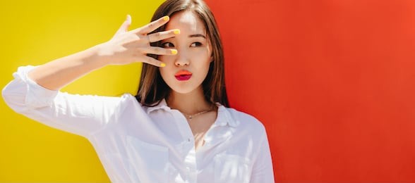 portrait of a woman standing outdoors against a colorful background. close up of a young woman wearing nail paint and lipstick looking away.