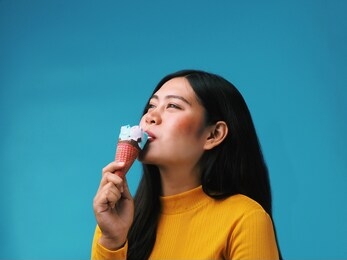 young beautiful woman holding ice cream cone over blue background.