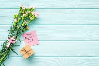 happy mother's day concept. hand lettering near bouquet of pink carnation and gift box on blue turquoise wooden background top view space for text