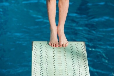 
legs of a young athlete in the starting position for jumping from a springboard of 3 meters in the indoor pool