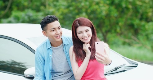 young couple take a selfie by smart phone happily with their car