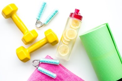 fitness set with bars, bottle of water, towel and wrist builder on white background top view