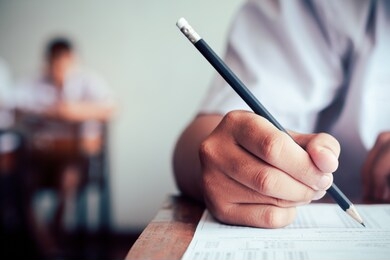 hand of student is taking exam and writing answer in classroom for education test concept