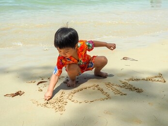young asian boy writing his name anda on the sands, playing on the beach during summer time. 