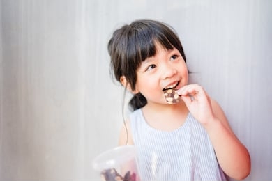 happy little asian girl child eating crispy brownie with almond and showing front teeth with big smile and laughing she have delicious.healthy happy funny smiling face adorable lovely female kid.