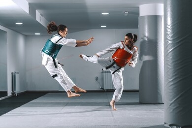 two caucasian young women sparring in taekwondo fittings in gym barefoot.