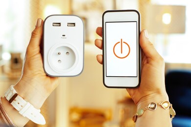 closeup on smartphone with smart home app and wifi smart plug in hands of modern woman in the house.