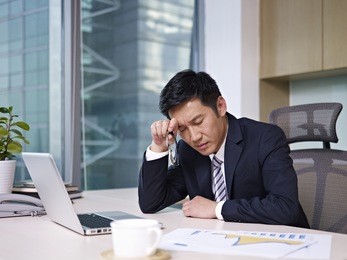 asian businessman sitting in office, looking tired.